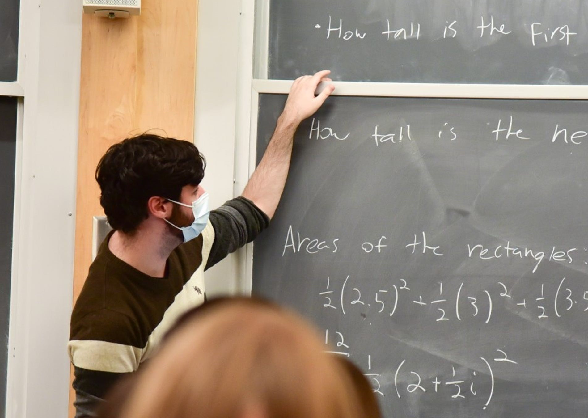 An instructor writing on a blackboard about rectangles of varying heights